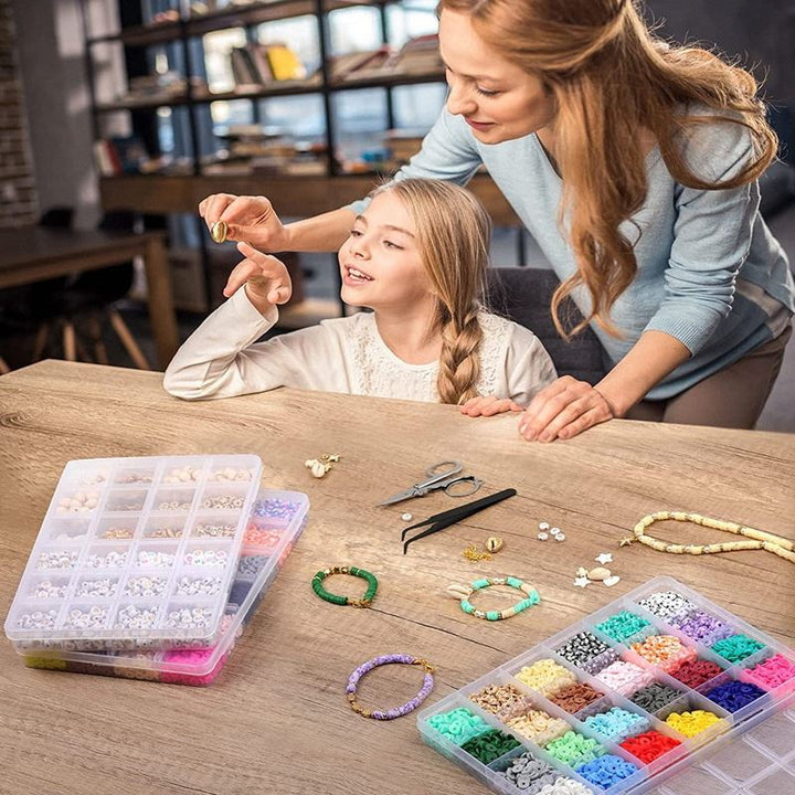 A woman and a young girl create bohemian jewelry at a table using the Fashiongirl Clay Beads / Heishi Beads Bohemian Kit, a KREA DIY Jewellery Kit with 6000 colorful beads and tools, in a cozy room with shelves behind them.