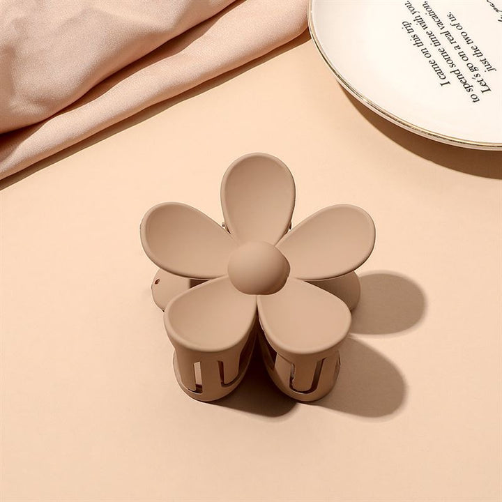 The SOHO Bloom Hair Claw - Brown by SOHO, featuring five petals, sits on a light beige surface next to a white plate with text and folded fabric.