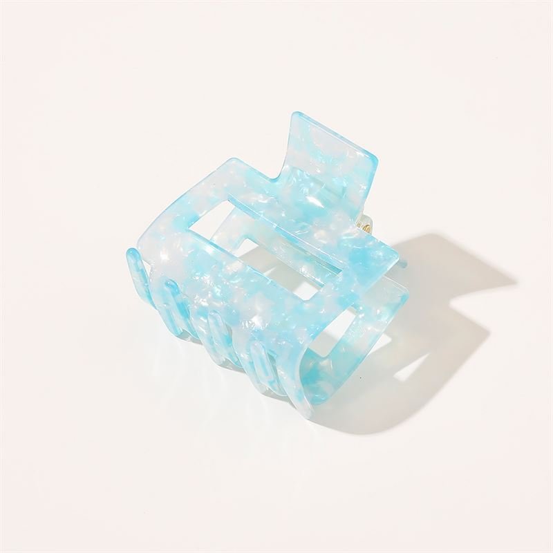 The SOHO Ema Hair Claw in Crystal Blue by SOHO features a translucent blue marbled design, shown on a white background with a soft shadow—a chic accessory ideal for elegant hairstyles.
