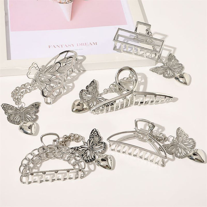 Six SOHO Emy Metal Hair Claw - Butterfly clips in metallic silver with butterfly and heart charms are arranged on a white surface. A pink and white FANTASY DREAM sheet is partially visible in the background.