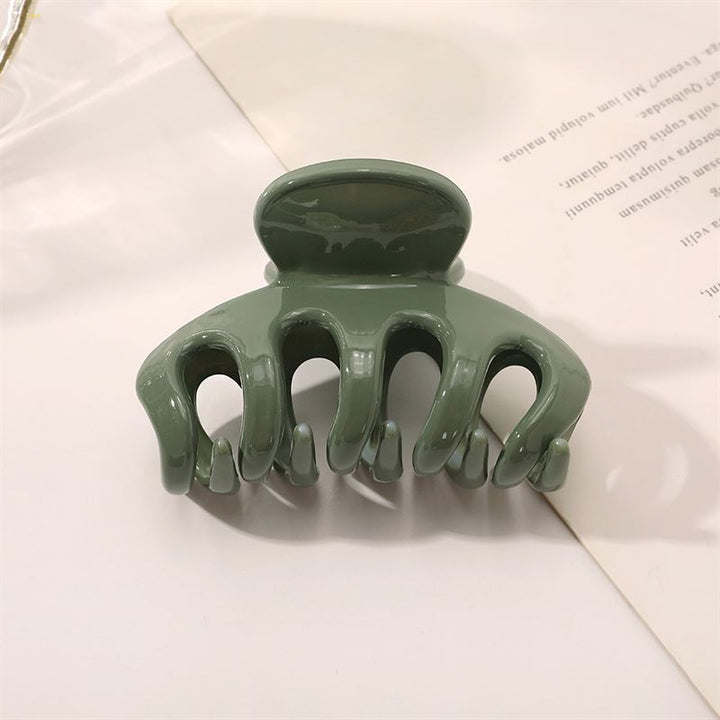 The SOHO Esta Hair Claw - Green by SOHO features curved prongs for extra grip, shown on a white surface next to a partially visible sheet of printed paper.