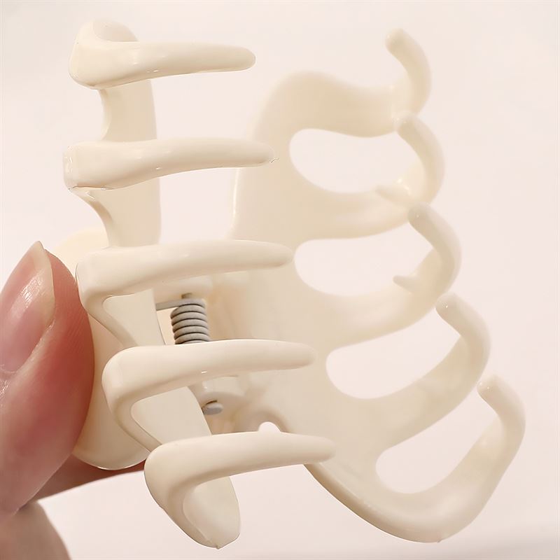 A close-up of a hand holding the SOHO Esta Hair Claw in green, featuring wide, curved prongs and a visible metal spring for secure hairstyling and extra grip.