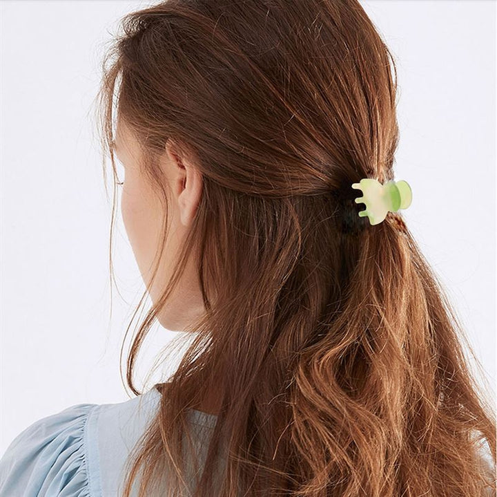 A woman with long brown hair in a low half ponytail, secured with the SOHO Hara Mini Hair Claw - Cloud Pink by SOHO, is shown from the back wearing a light blue top.