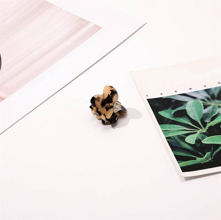 The SOHO Hara Mini Hair Claw - Light Tortoise by SOHO sits on a white surface next to two open magazines, one with green plant leaves, providing a stylish and secure grip for your hair.