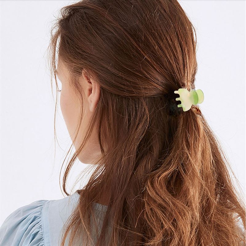 A woman with long brown hair, seen from behind, wears a pale blue top and secures her half-up hairstyle with the SOHO Hara Mini Hair Claw in Porcelain by SOHO.