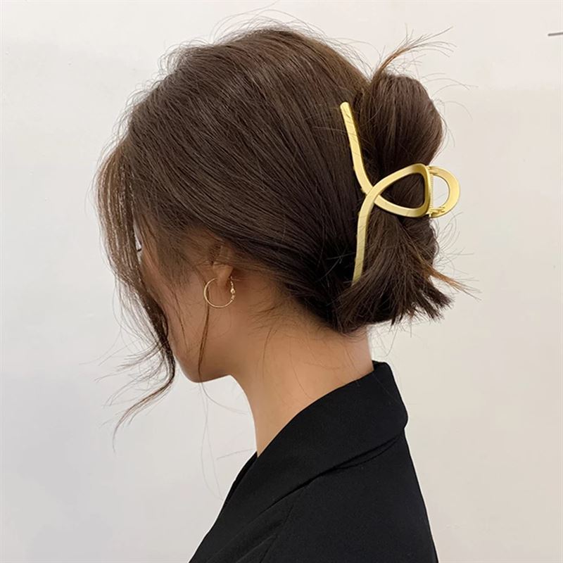 A woman with brown hair in a low messy bun, secured by the SOHO Iva Metal Hair Claw in Silver, wears a black top and small hoop earring. She is shown from the side against a plain background.