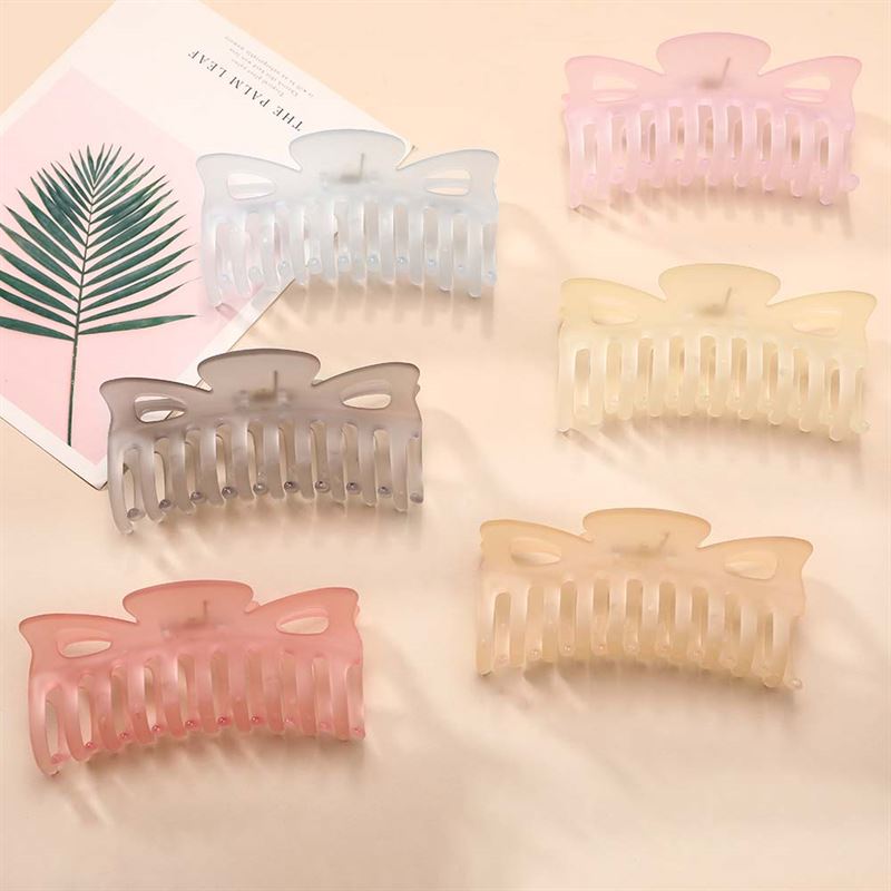 The SOHO Jelly Hair Claw in beige, from the brand SOHO, offers a strong grip for all hair types. It is shown neatly arranged on a light surface next to a book with a palm leaf cover.
