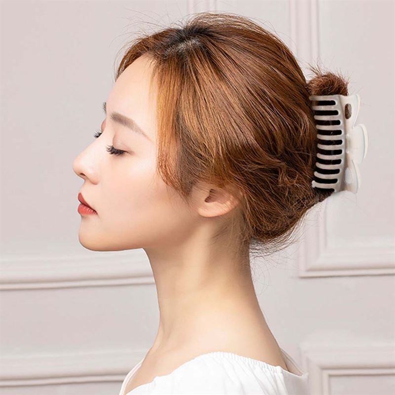 A woman with light brown hair in a neat bun, secured by the SOHO Jelly Hair Claw - Cloudy Grey, is shown in profile against a light-paneled background. Designed by SOHO, this claw offers a strong grip and suits all hair types.