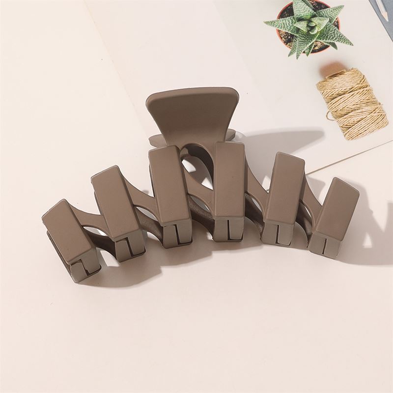 The SOHO Just Hair Claw - Brown by SOHO is displayed on a light surface next to a small potted succulent and a spool of twine.