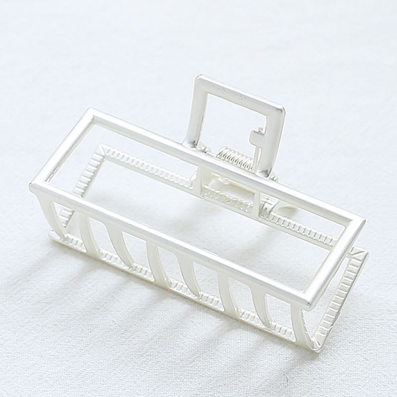 The SOHO Kai Small Metal Hair Claw in matte silver, featuring a geometric open-frame design, rests on a white surface—perfect for securing your hairstyle.