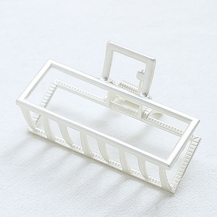 The SOHO Kai Small Metal Hair Claw in matte silver, featuring a geometric open-frame design, rests on a white surface—perfect for securing your hairstyle.