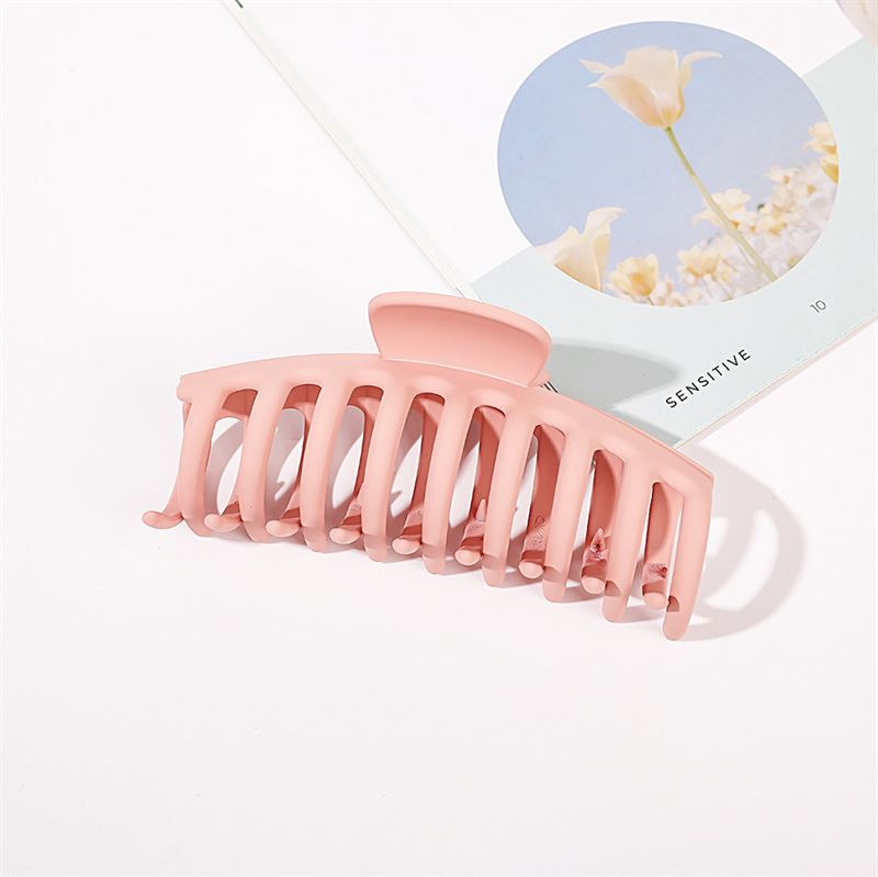 The SOHO Kana Hair Claw in Peach Beige rests on an open book with a floral image and the word "SENSITIVE." Its strong grip suits all hair types. A white background enhances the clean, minimalistic style.