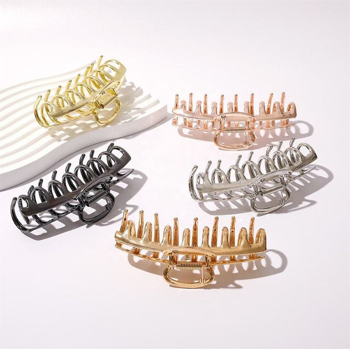 Five large SOHO Kana Metal Hair Claw clips in gold, rose gold, silver, bronze, and black are arranged on a white surface. A white tray in the background holds the SOHO Kana Metal Hair Claw - Gold.