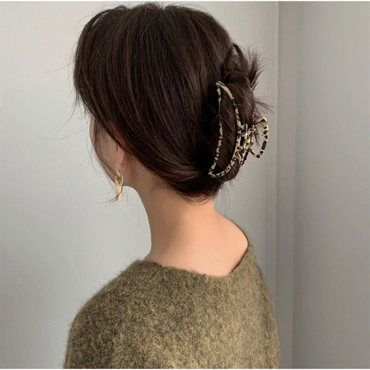 A woman with brown hair in a loose updo, secured by the SOHO Leopard Metal Barette Hair Claw, wears a fuzzy olive sweater and gold earrings. She faces away from the camera, highlighting her SOHO hair accessory.