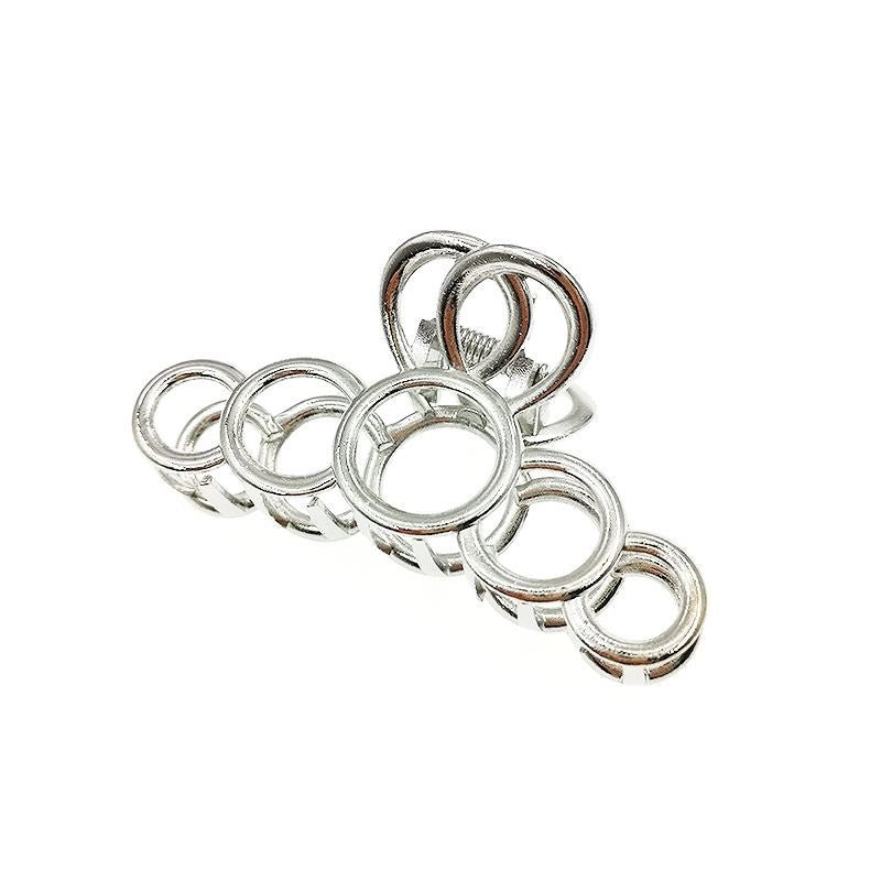 Seven shiny metal rings of varying sizes, inspired by the elegant curves of the SOHO Metal Hair Claw - Silver from SOHO, are arranged in a line like a caterpillar on a white background.