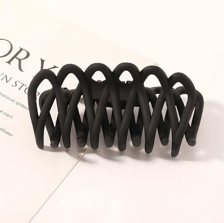 The SOHO Olive Hair Claw - Black by SOHO features a matte finish and interlocking curved prongs for a gentle grip, perfect for securing all hair types—shown resting on an open magazine with visible text on a white background.