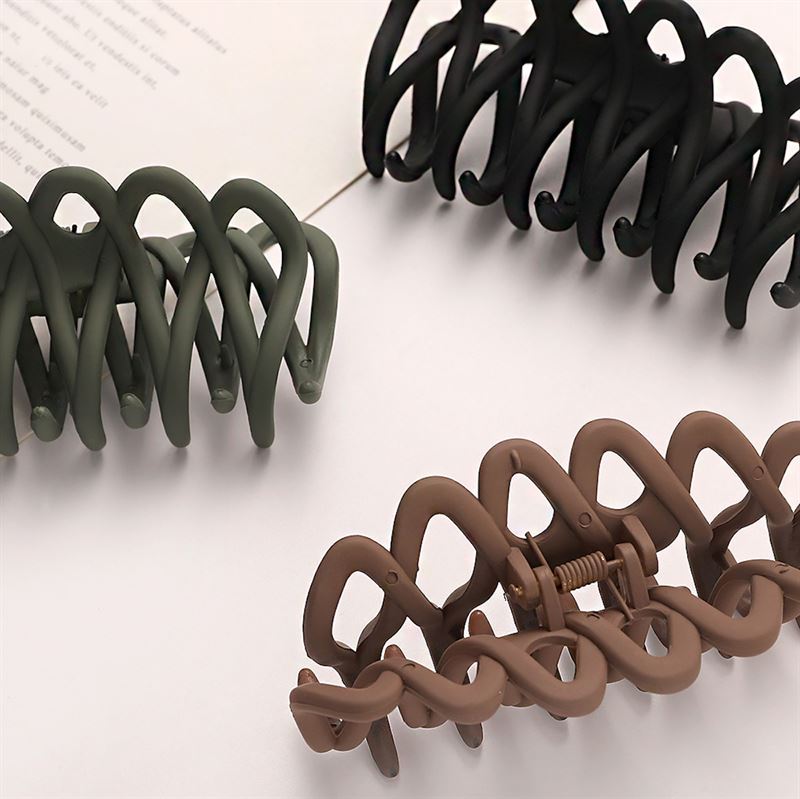 The SOHO Olive Hair Claw - Brown by SOHO, with a matte finish and visible spring, features a wavy interlocking design that provides a gentle grip for all hair types. It rests stylishly on a light surface beside an open book.