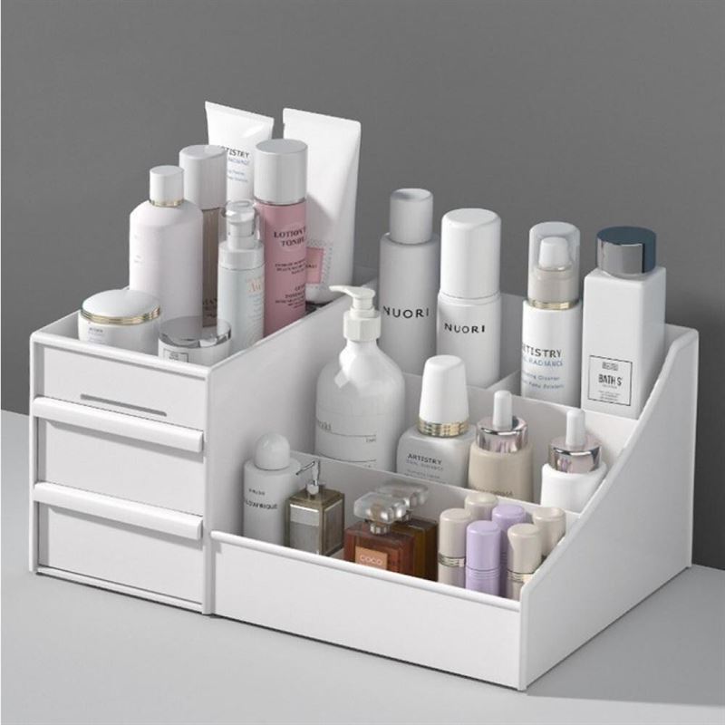 The UNIQ Cosmetic Organiser with Two Drawers, White - P110 neatly stores skincare and makeup bottles, jars, and tubes in its compartments. This white organiser by UNIQ is displayed on a grey surface against a grey wall.