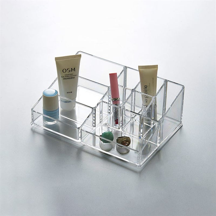 The UNIQ Make Up Acrylic Organiser - SF-1611D (U304) by UNIQ neatly arranges tubes of cream, a stick, lipstick, lip balm, and round containers in clear compartments on a light surface.