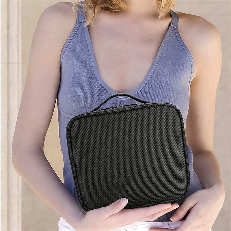 A woman in a sleeveless, light purple top holds the UNIQ makeup travel bag—a black, rectangular cosmetic bag with adjustable compartments and a handle—in front of her torso.