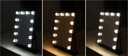 The UNIQ New York Mega Makeup Mirror by UNIQ, featuring 12 exposed bulbs and touch controls, is shown in black with warm, neutral, and cool lighting modes illuminating a dark room.