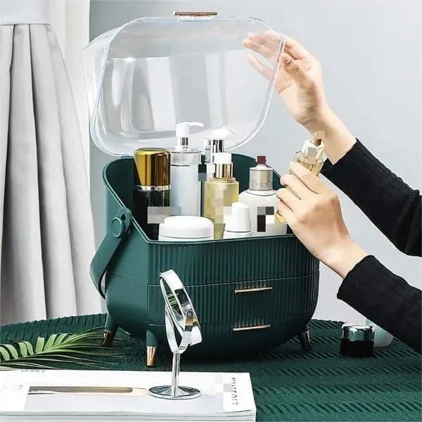 Someone organizes skincare and cosmetics in the UNIQ Retro Makeup Box Organiser (Dark Mint/Dark Green) by UNIQ, featuring a clear lid, set on a green tablecloth with a small round mirror and extra beauty items nearby.